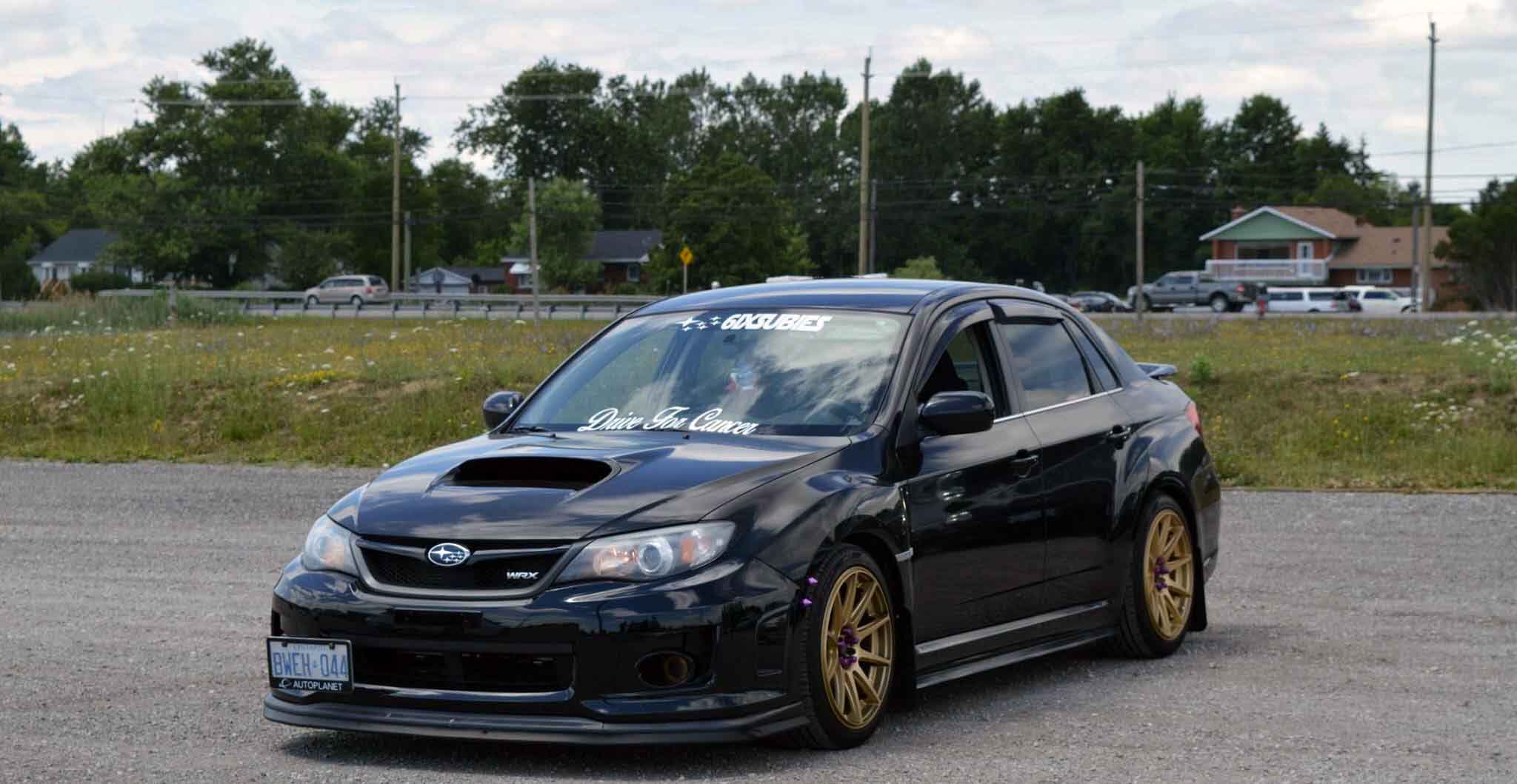 Black Subaru WRX with Drive For Cancer windshield banner at a community car meetup